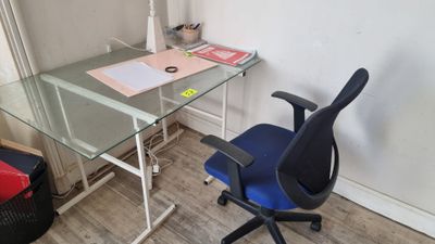 un bureau en verre avec une chaise bleue devant