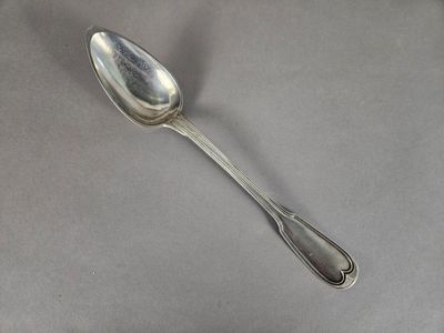 une cuillère en argent posée sur une surface grise, à côté d'une feuille de papier
