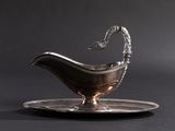 a silver sauce boat on a silver plate on a black background