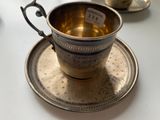 a silver cup and saucer sitting on a saucer