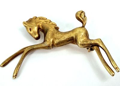 gold plated horse broochle on white surface with white background