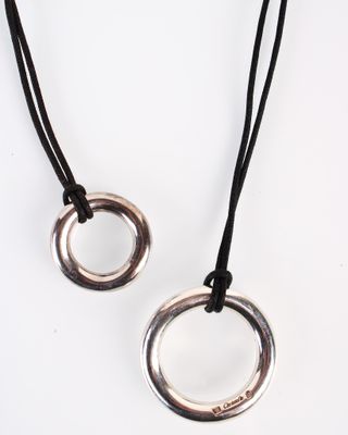 deux bagues en argent sur un collier à cordon noir, sur fond blanc