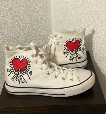 une paire de baskets blanches ornées d'un cœur rouge, posée sur une table en bois