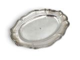 an oval silver plate with a scalloped edge on a white surface