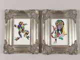 pair of silver picture frames with colorful paintings on them on a white surface
