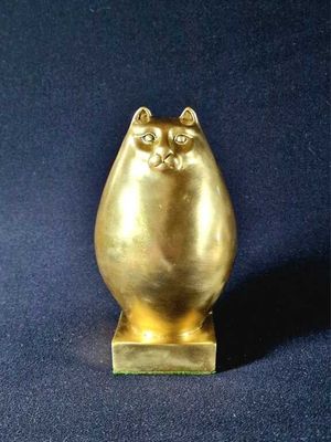 brass cat figurine on stand on dark blue background