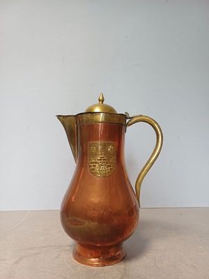 an antique copper coffee pot with a brass handle on a table