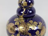 un vase bleu orné de fleurs dorées, posé sur un fond blanc