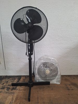 un ventilateur noir posé sur un parquet, près d'un mur blanc