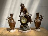 trois statues en bronze représentant une femme assise sur une horloge