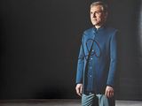 une vieille photo d'un homme en costume bleu, debout devant un mur noir