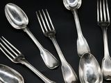 a lot of silver spoons and forks on a black table