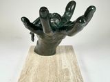 a statue of a hand holding a green object on top of a wooden base