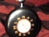une montre de poche noire posée sur une couverture rouge, entourée d'un anneau doré