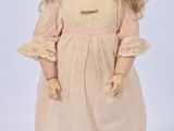 an antique doll with blonde hair and blue eyes standing on a white surface