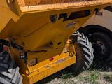 a yellow dump truck parked in a field with a white truck behind it