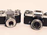 two old cameras sitting side by side on a white surface