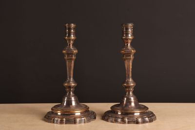 une paire de bougeoirs anciens en laiton posés sur une table, sur fond noir
