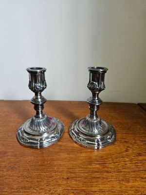 une paire de bougeoirs en argent posés sur une table en bois, avec un mur blanc en arrière-plan