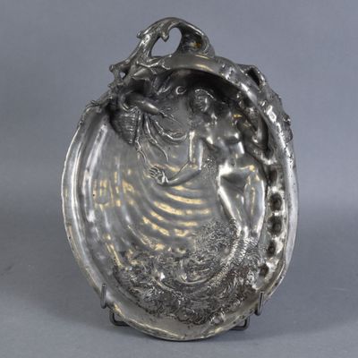 une assiette ancienne en argent sur laquelle est représentée une femme en robe