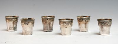 six verres à shot en argent alignés en rangée sur une surface blanche