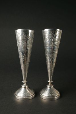 une paire de vases en argent posés sur une surface noire, sur fond noir