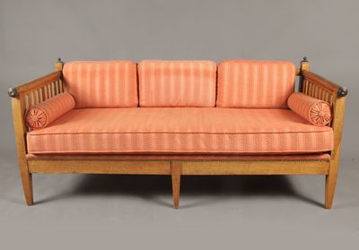 un canapé rayé orange, avec une structure en bois et des accoudoirs, sur fond gris