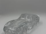une image représentant une petite voiture en verre transparent posée sur une surface blanche