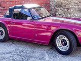 a pink convertible car parked in front of a brick wall