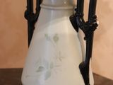 a white vase with a black handle on a table next to a lamp