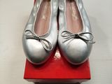 une paire de chaussons de danse argentés posés sur une boîte rouge, elle-même posée sur une surface blanche