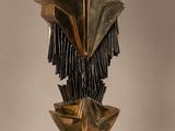 sculpture représentant une tête en bronze ornée de franges, posée sur un socle en bois