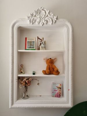 une étagère blanche sur laquelle sont posés un ours en peluche et des livres