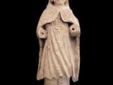 une vieille statue représentant une femme coiffée d'un chapeau et vêtue d'une robe
