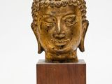 une tête de Bouddha en or posée sur un socle en bois, sur fond blanc