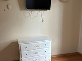 une commode blanche dans une pièce où est accrochée une télévision à écran plat au mur