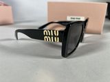 the sunglasses are black with gold letters on them and a pink box in the background