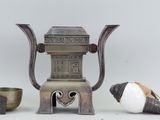a silver teapot with a bird next to it and a bowl