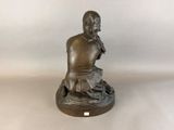 a bronze statue of a man sitting on a rock with a bird in his hand