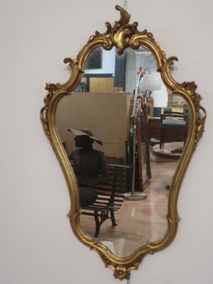 a mirror hanging on the wall with a man sitting on a bench in front of it