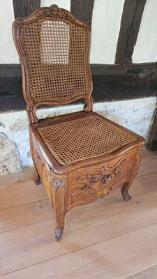 une chaise en bois avec une assise en osier, posée sur un plancher en bois