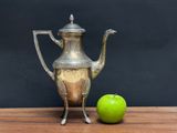 a silver tea pot next to an apple on a wooden table