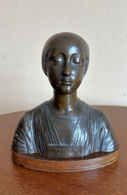 bronze bust of a woman on a wooden table with a white wall in the background