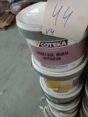 Plusieurs seaux de peinture sont empilés les uns sur les autres dans un entrepôt