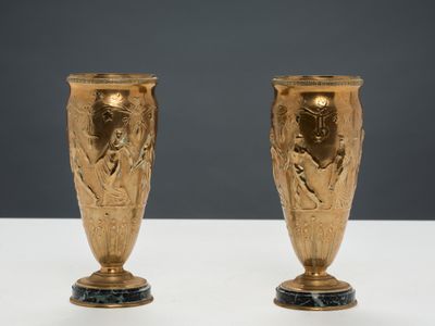une paire de vases en or posés sur une table blanche, sur fond gris