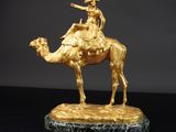 statue en or représentant un homme à dos de chameau, posée sur un socle en marbre