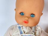 a baby doll with blue eyes sitting on a white surface