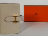 une photo d'un portefeuille blanc orné d'une boucle dorée et d'une boîte orange
