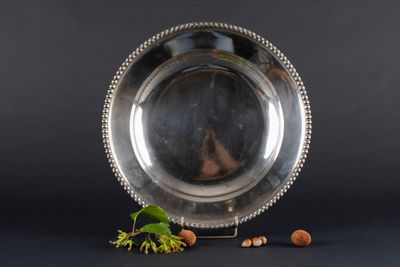 an antique silver plate with beading and nuts on a black background
