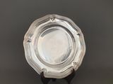 un plat ancien en argent posé sur un socle, sur fond gris